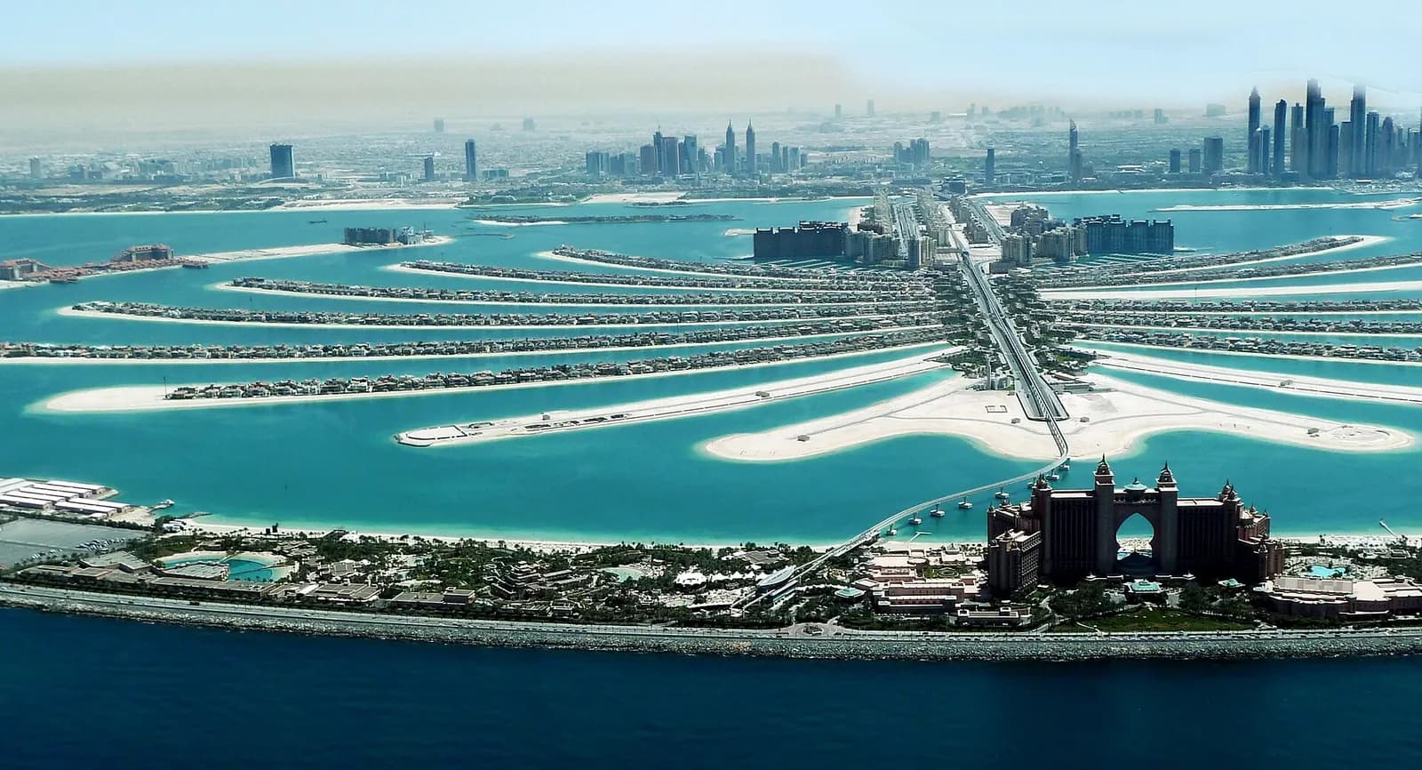 Aerial daytime view of Palm Jumeirah with the trunk in the middle, the fronds on both sides, the crescent in front and Atlantis, The Palm at the crescent apex.