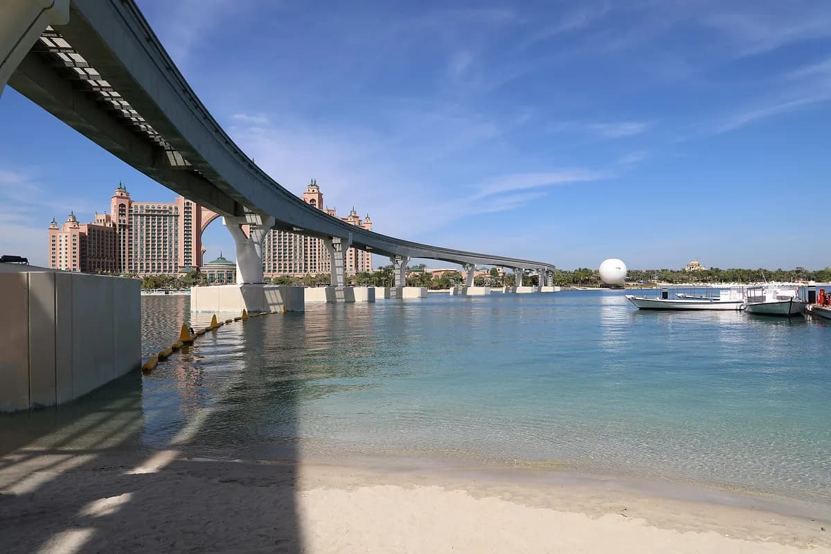 The Palm Monorail track curving over shallow water and a beach toward the towers of Atlantis, The Palm under a blue sky.
