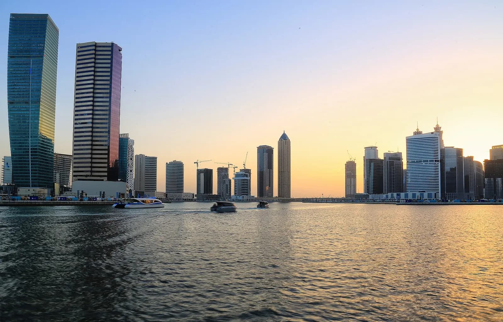 Towers along the Dubai Water Canal in Business Bay at sunset, with a water taxi passing